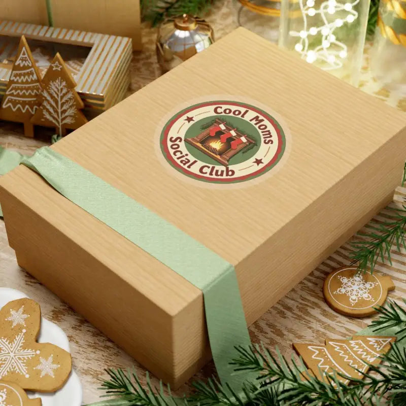 Gift box with ribbon beside Cool Moms Social Club Holiday Sticker featuring fireplace and stockings