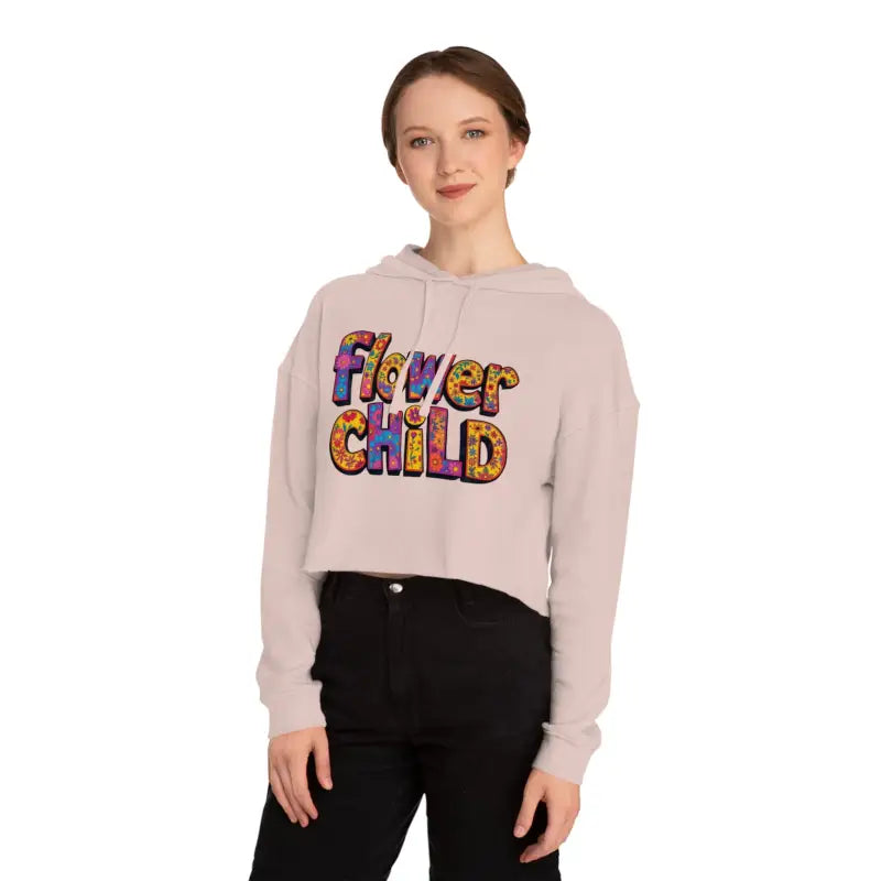 Woman wearing a light pink cropped hoodie with Flower Child in colorful patterned letters