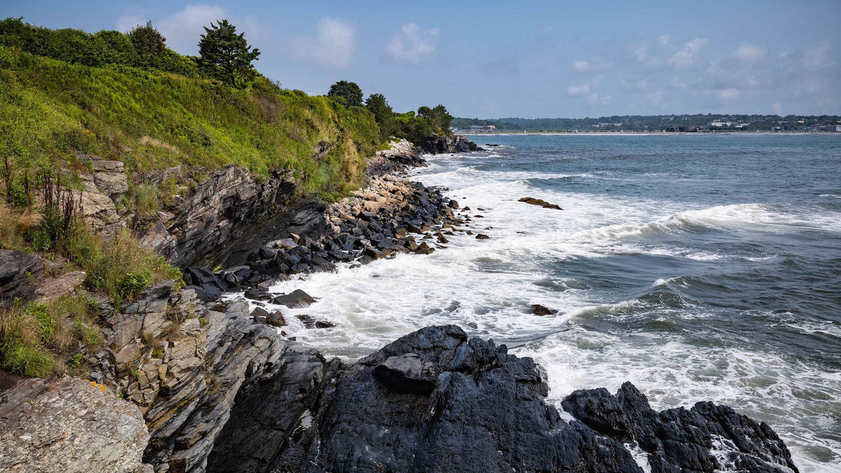 Rocky Newport Rhode Island coastline with waves and green cliffs.
